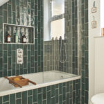 A beautiful newly renovated bathroom with emerald green metro tiles, a shower over a bath and geometric floor tiles