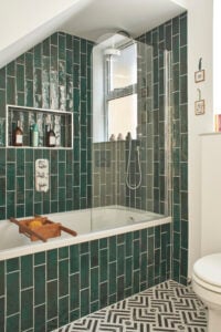 A beautiful newly renovated bathroom with emerald green metro tiles, a shower over a bath and geometric floor tiles